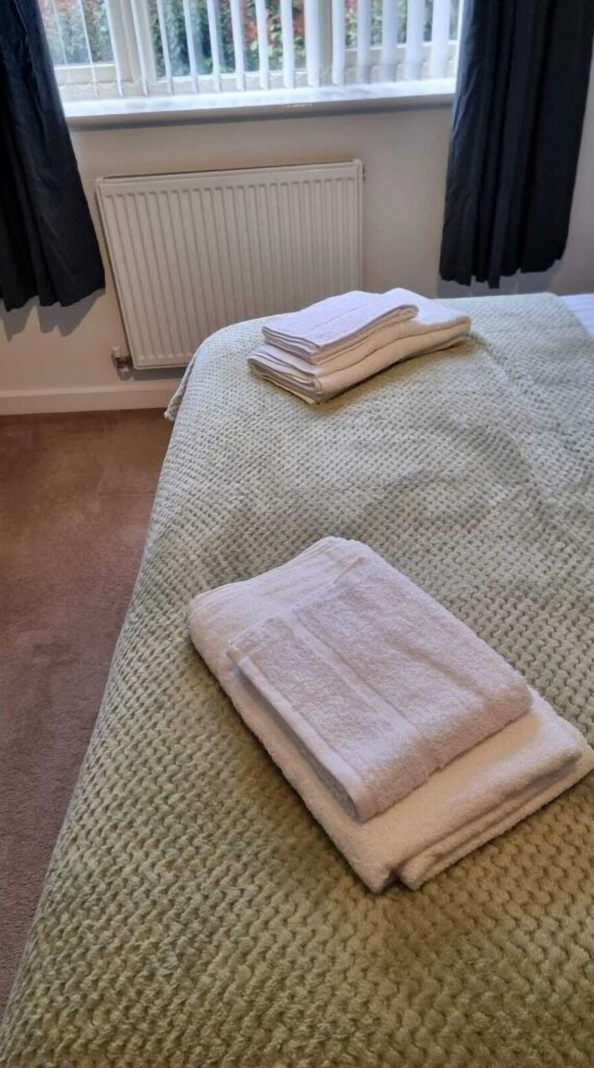 Ein Bett mit einer grünen, gestrickten Tagesdecke und gefalteten Handtüchern.