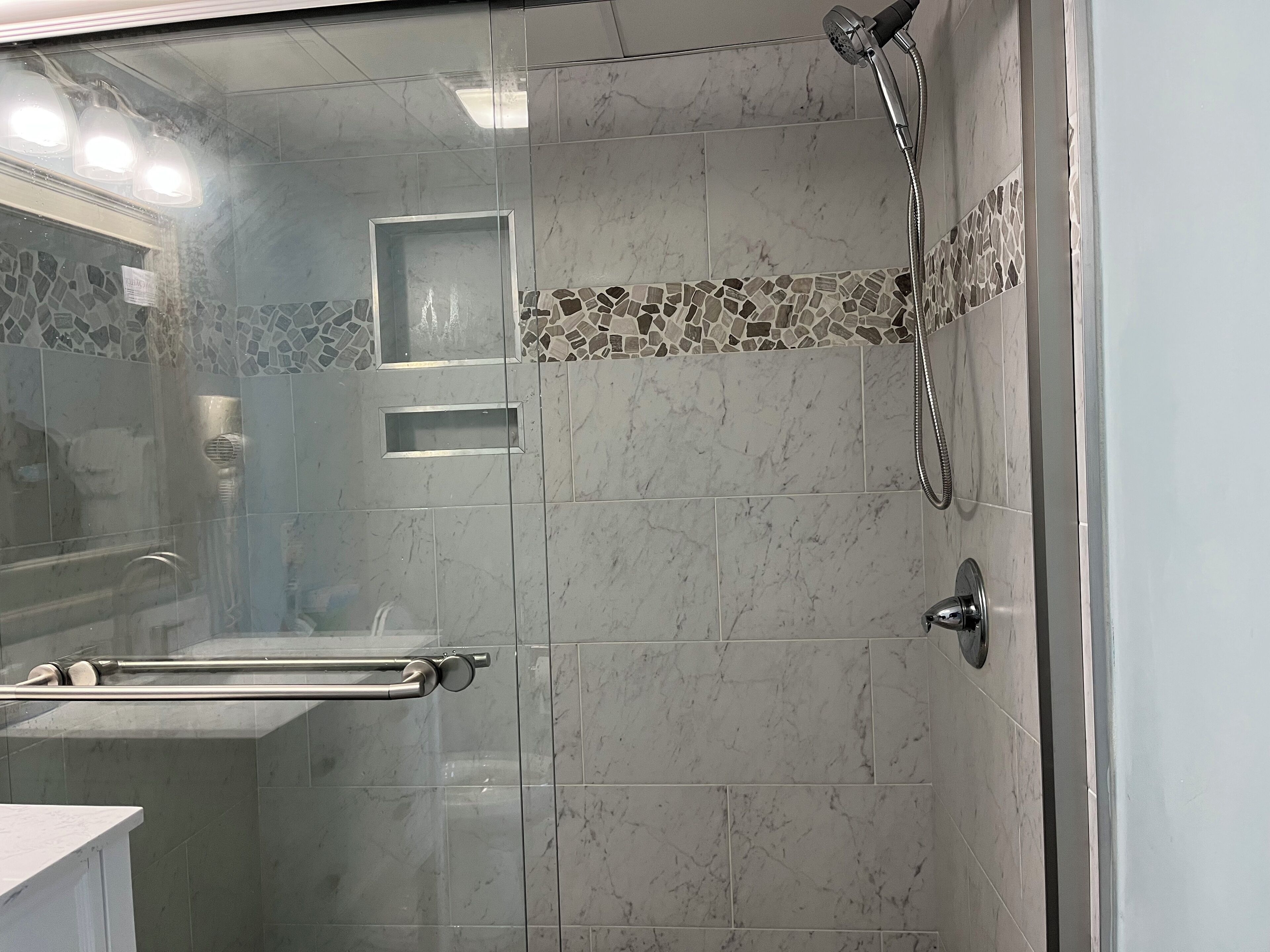A modern bathroom with a glass shower enclosure, a handheld showerhead, and a towel rack.