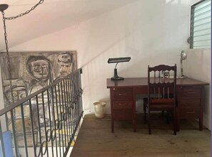 Una stanza con una scrivania in legno, due sedie, una lampada da scrivania e un quadro appeso al muro.