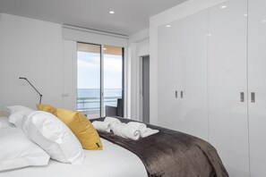 Ein modernes Schlafzimmer mit Bett, Meerblick durch eine Schiebetür und einem Kleiderschrank.