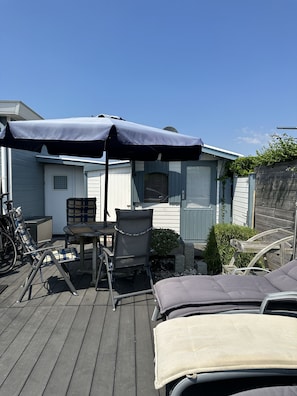 Eine Terrasse mit Gartenmöbeln, darunter ein Tisch und Stühle, sowie ein überdachter Bereich mit Sonnenschirm.