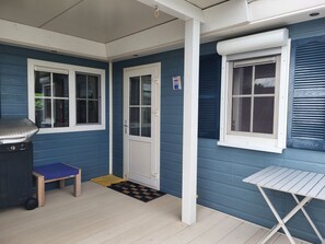 A covered porch with a grill, a small wooden bench, a door, and a window with a view. - NV 206 - Beach Resort Nieuwvliet Bad (Nieuwvliet)