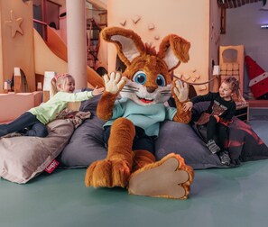 Suuri, pehmeä kanimaskotti huoneessa, jossa on tähtimäinen seinäkoriste, liukumäki ja sydämenmuotoinen tyyny.