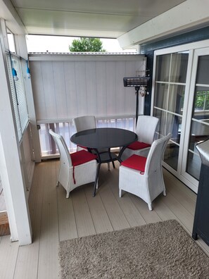 Ein überdachter Patio-Bereich mit einem runden Tisch und vier Stühlen, einem Deckenventilator und einer Schiebetür.