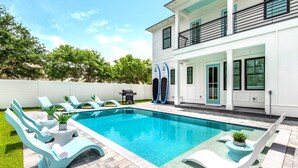 Une maison moderne à deux étages dotée d’une piscine, d’un espace extérieur aménagé et d’un coin barbecue.