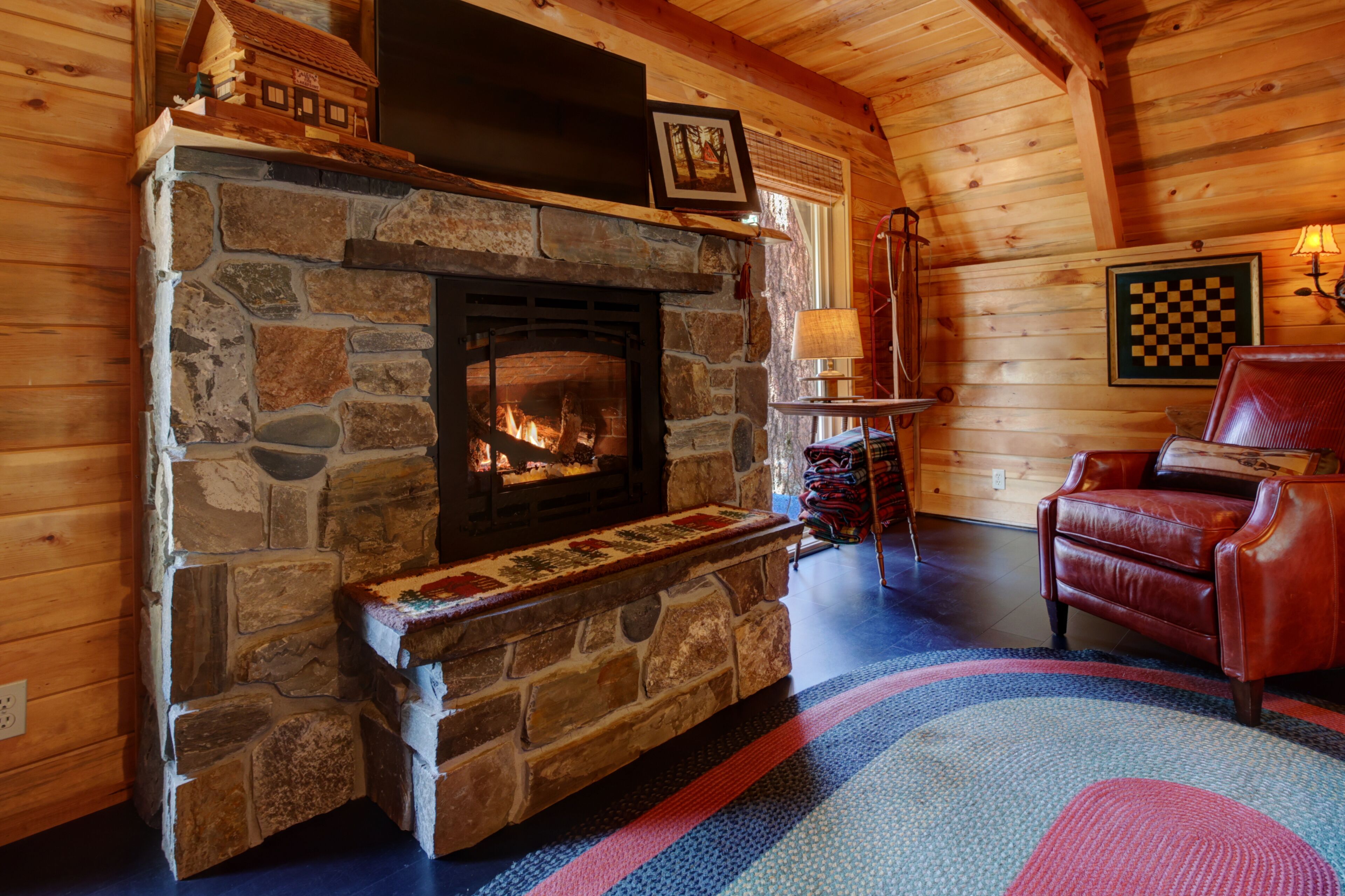 A stone fireplace with a fire, a red leather chair, and a checkered wall art piece.