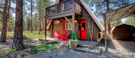 Una cabana amb un porxo, una porta vermella i dues cadires Adirondack vermelles.