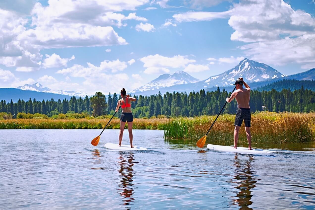 Two people paddleboarding on a calm lake with a mountain in the background.