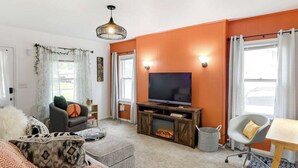 Sala de estar con televisión, sofá y sillón, paredes anaranjadas y chimenea.