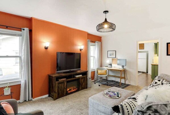 A living room with a TV, a fireplace, a desk with a computer, and a sofa.