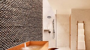 Un bagno moderno con una vasca da bagno in legno, un muro in pietra, uno sgabello in legno e un porta asciugamani.