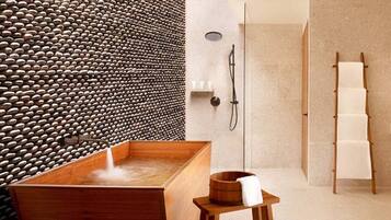 Un baño moderno con una bañera de madera, una pared de piedra, un taburete de madera y un perchero para toallas.