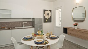 A modern kitchen with white cabinets, a dining table set for four, and a large flower painting on the wall. - San Carlo Borromeo 1 by Wonderful Italy (Soiano del Lago)