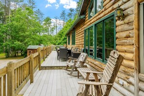 Une cabane en rondins dotée d’une terrasse, de meubles de jardin et offrant une vue sur la forêt.