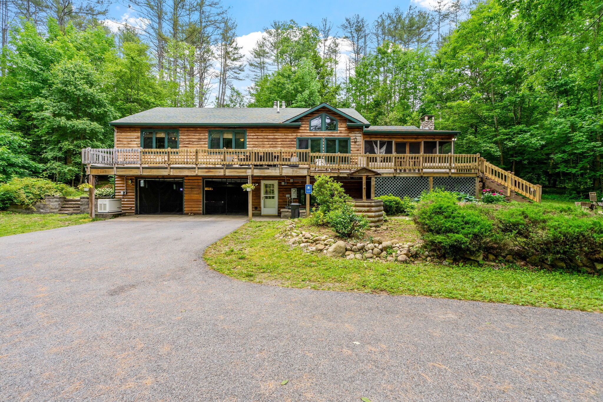 A log cabin with a covered porch, a garage, and a stone foundation.