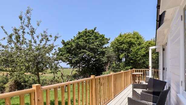 Une terrasse en bois avec des meubles d’extérieur, une vue sur les arbres et un champ d’herbe.