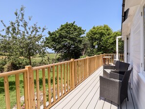Une terrasse en bois avec des meubles d’extérieur, une vue sur les arbres et un champ d’herbe.