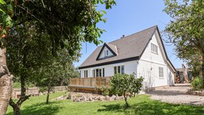 Une maison blanche avec un toit foncé, entourée d’une pelouse bien entretenue et d’arbres.