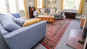 Un salon avec un canapé bleu, un canapé gris, une table basse en bois et un tapis à motifs.