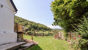 Une maison à l’extérieur blanc, avec un chemin de briques menant à la porte d’entrée et une terrasse en bois.