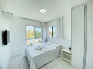 Quarto com cama, mesa de cabeceira, televisão na parede e janela com cortinas.