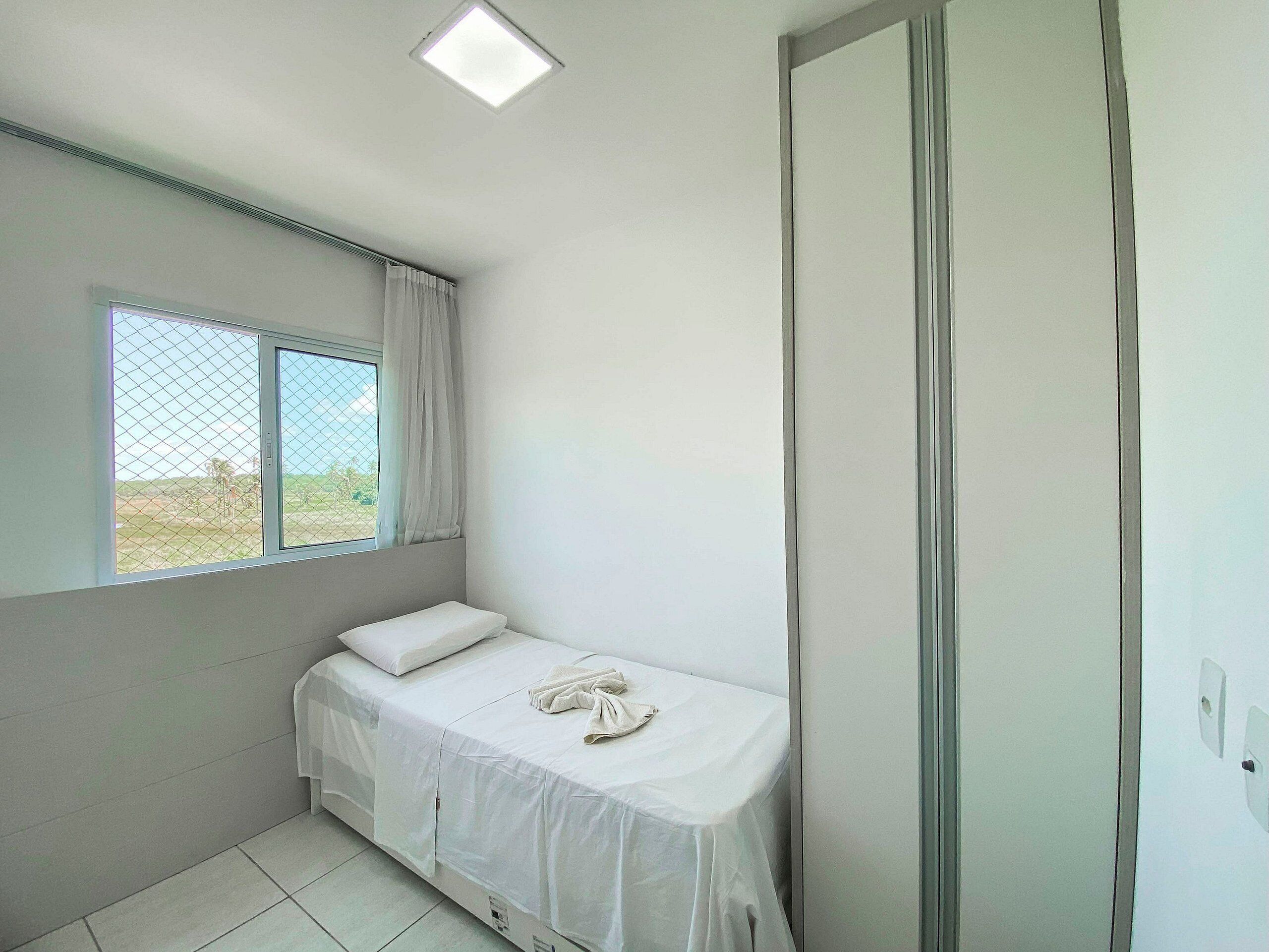 Une petite chambre avec un lit simple, une fenêtre, une porte et un luminaire au plafond.