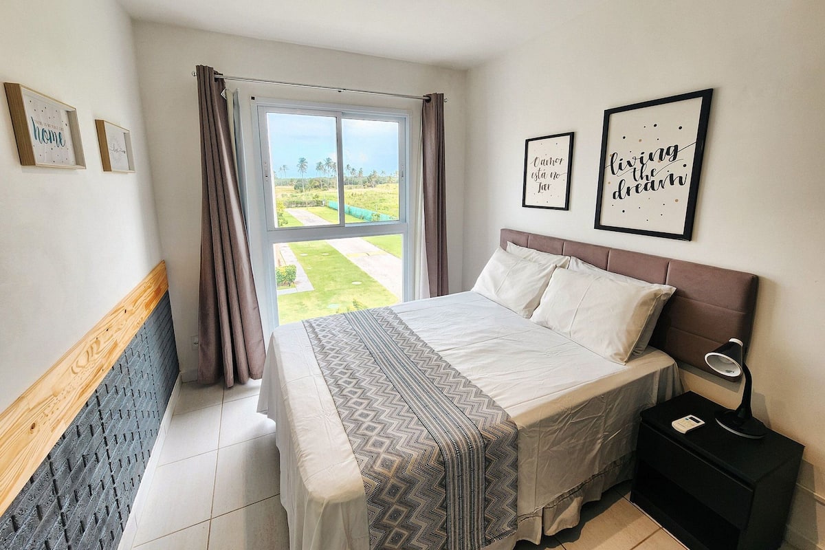 A bedroom with a bed, a nightstand, a window with curtains, and two framed motivational quotes on the wall.