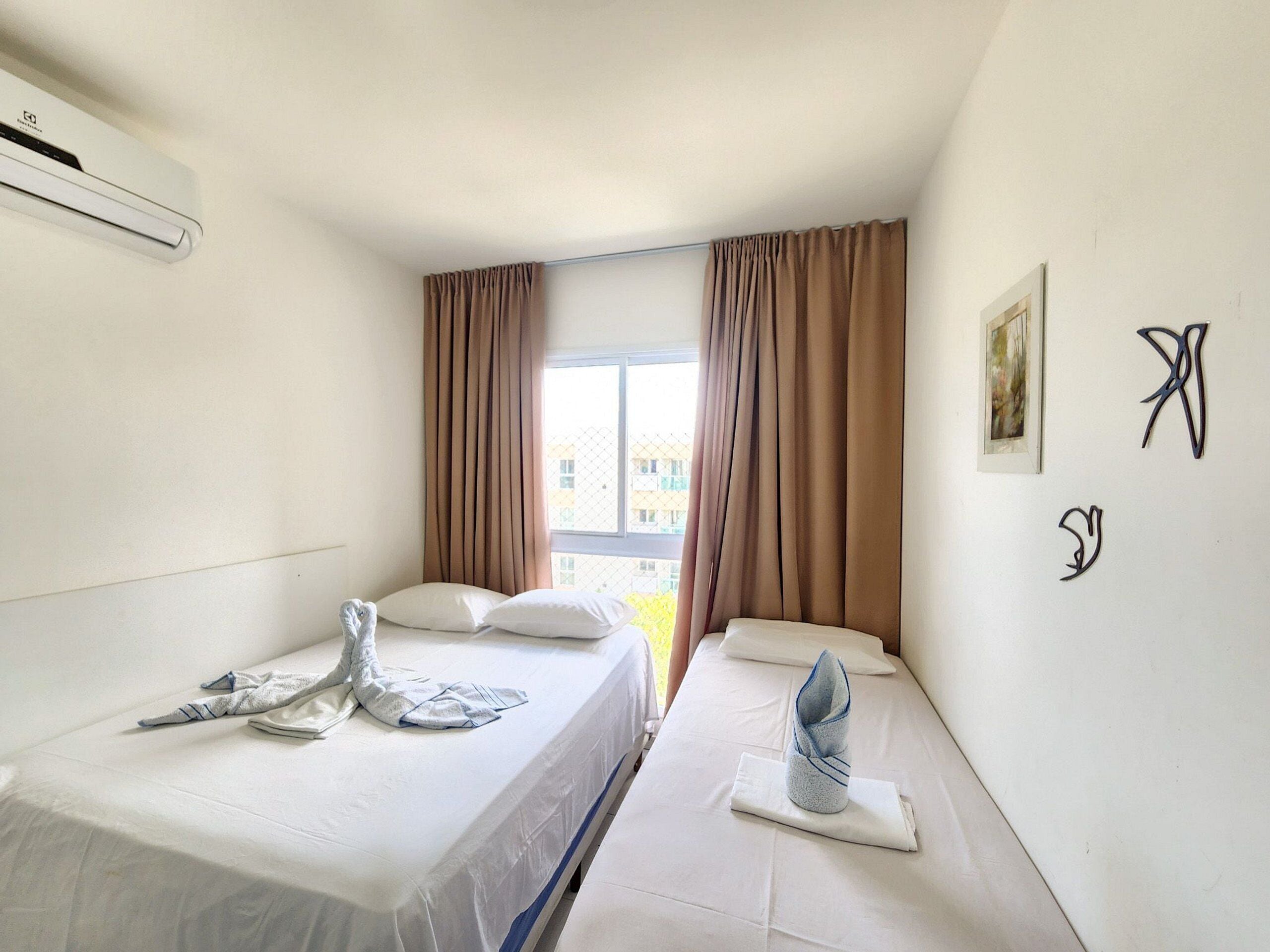 Habitación de hotel con dos camas, una ventana con cortinas, un equipo de aire acondicionado y un cuadro abstracto en la pared.