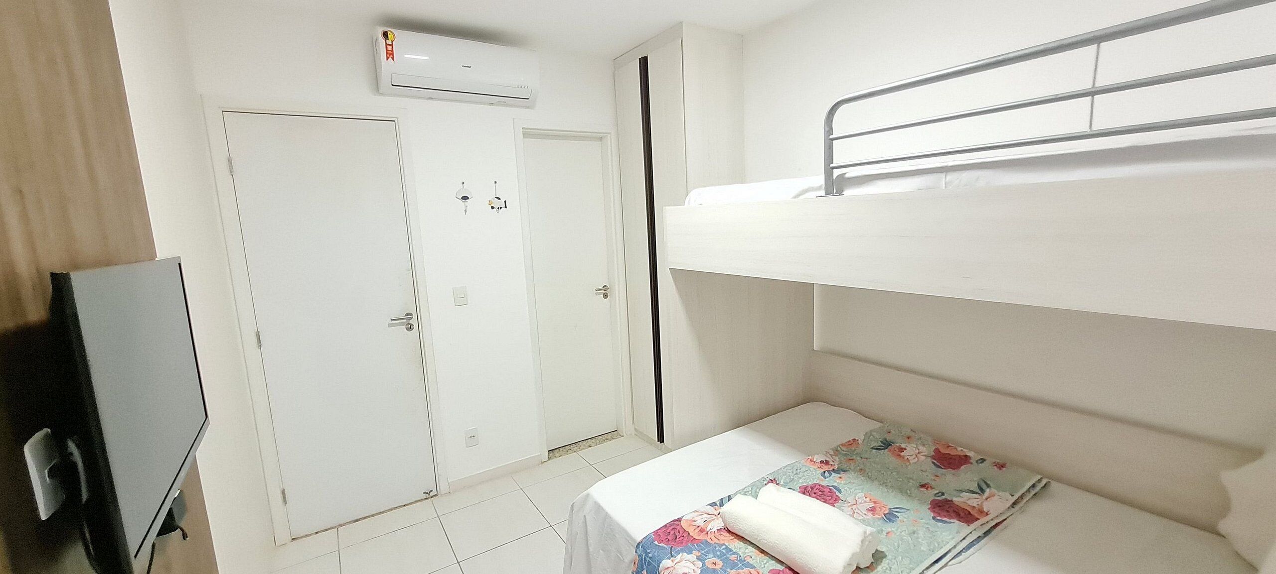 A room with a bunk bed, a desk with a chair, a wardrobe, and an air conditioning unit.
