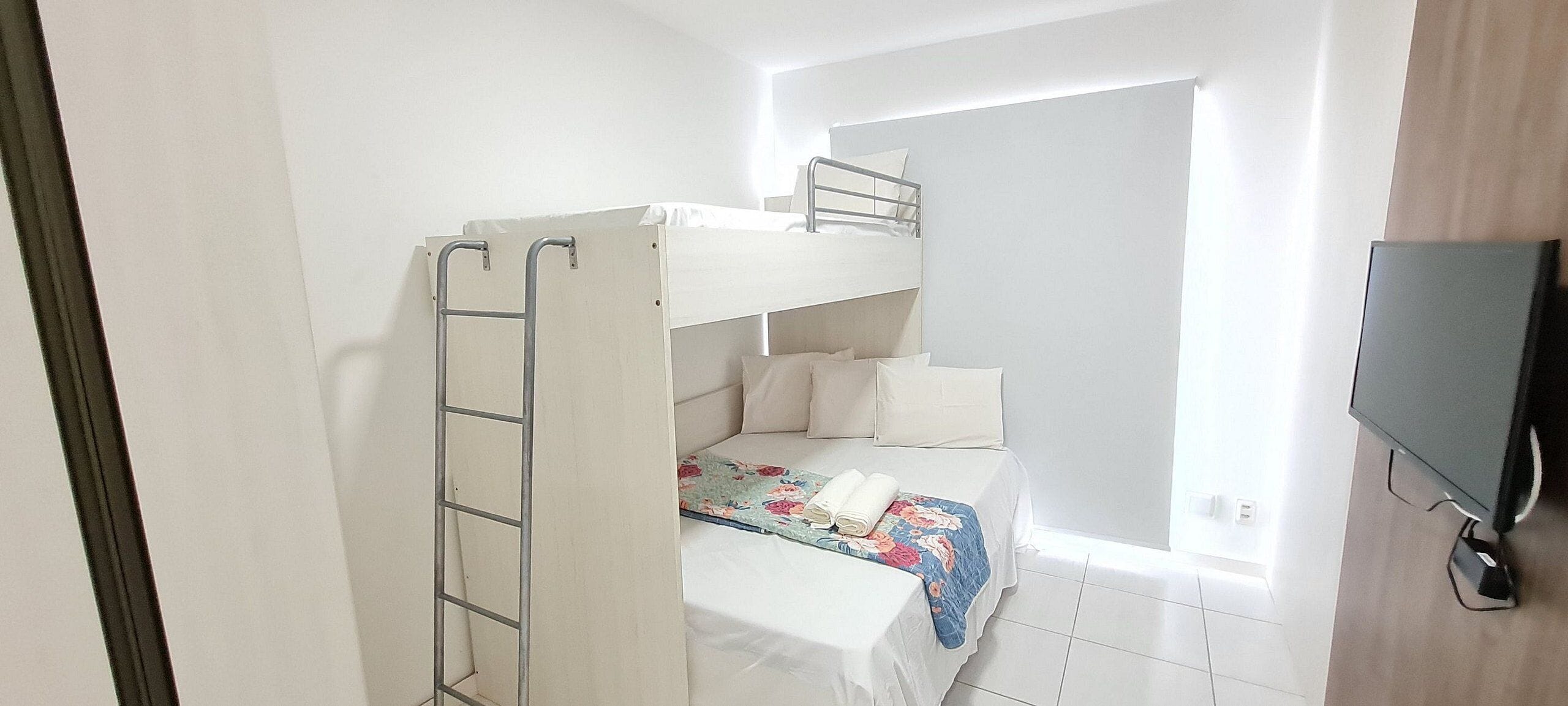 A bunk bed room with a ladder, a television, and a window.