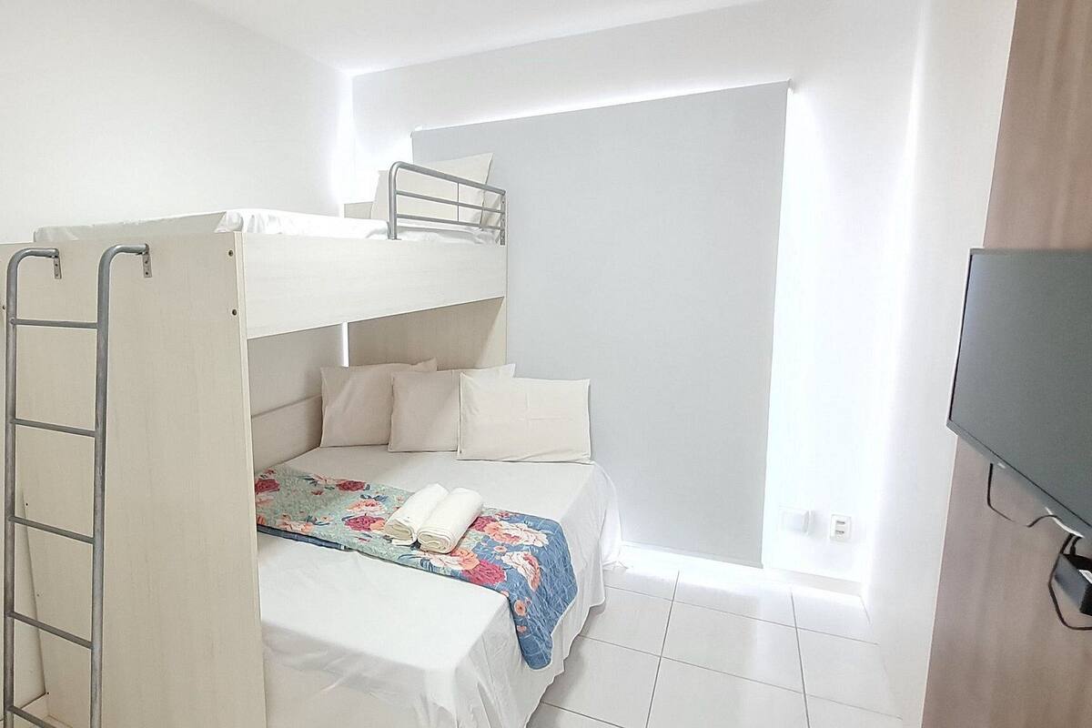 A bunk bed room with a ladder, a television, and a window.