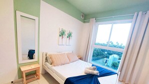 A bedroom with a bed, a small bedside table, a window with curtains, and a mirror on the wall. - Flats no Muro Alto Condomínio Club (Ipojuca)