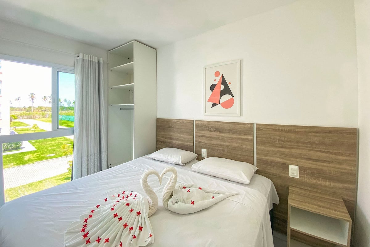 A hotel room with a bed, a wardrobe, a window with a view, and a framed picture on the wall.