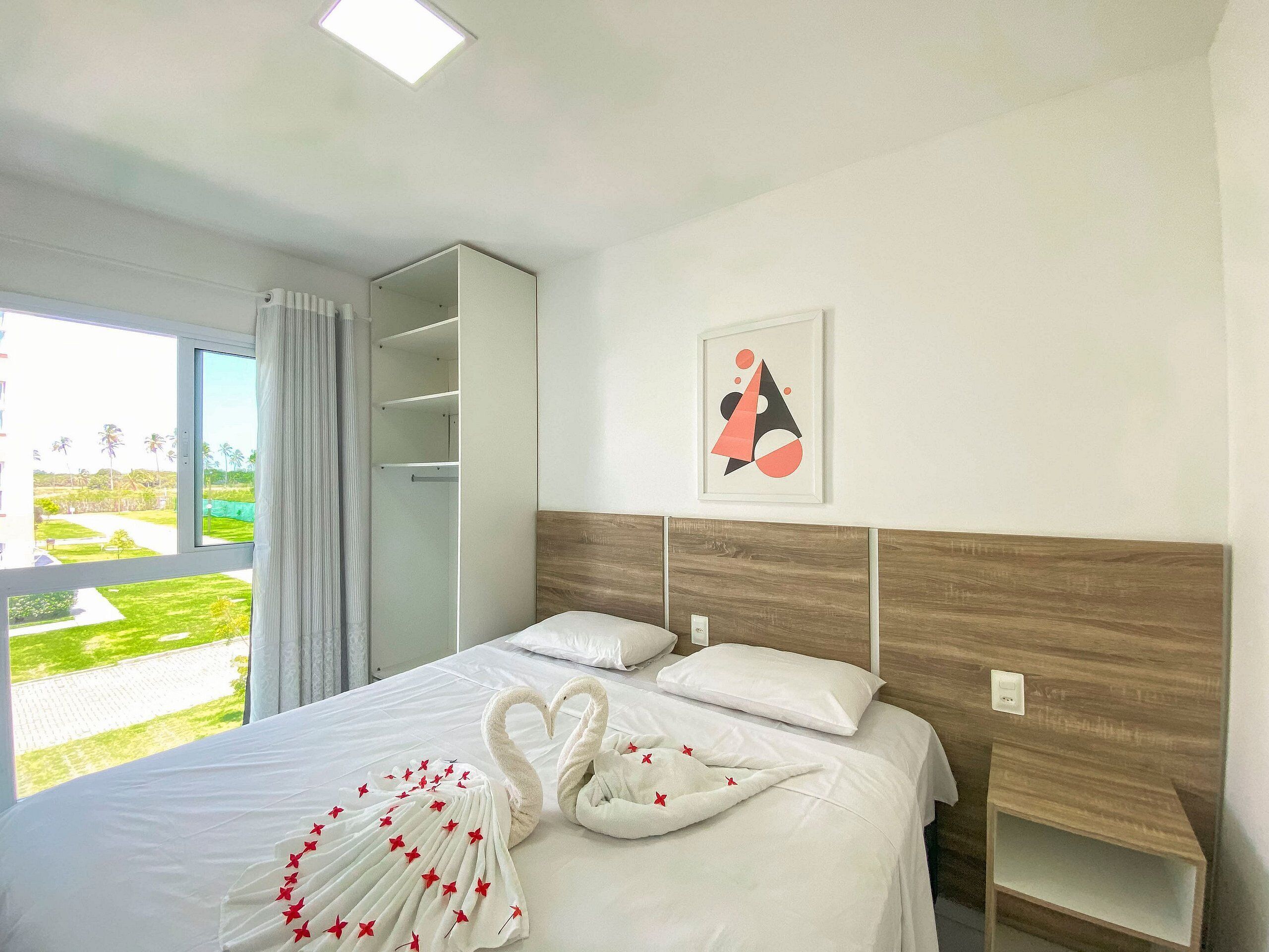 Quarto de hotel com cama, guarda-roupa, janela com vista e um quadro na parede.