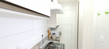 A kitchen with white tiles, a stove, a toaster, and a microwave.