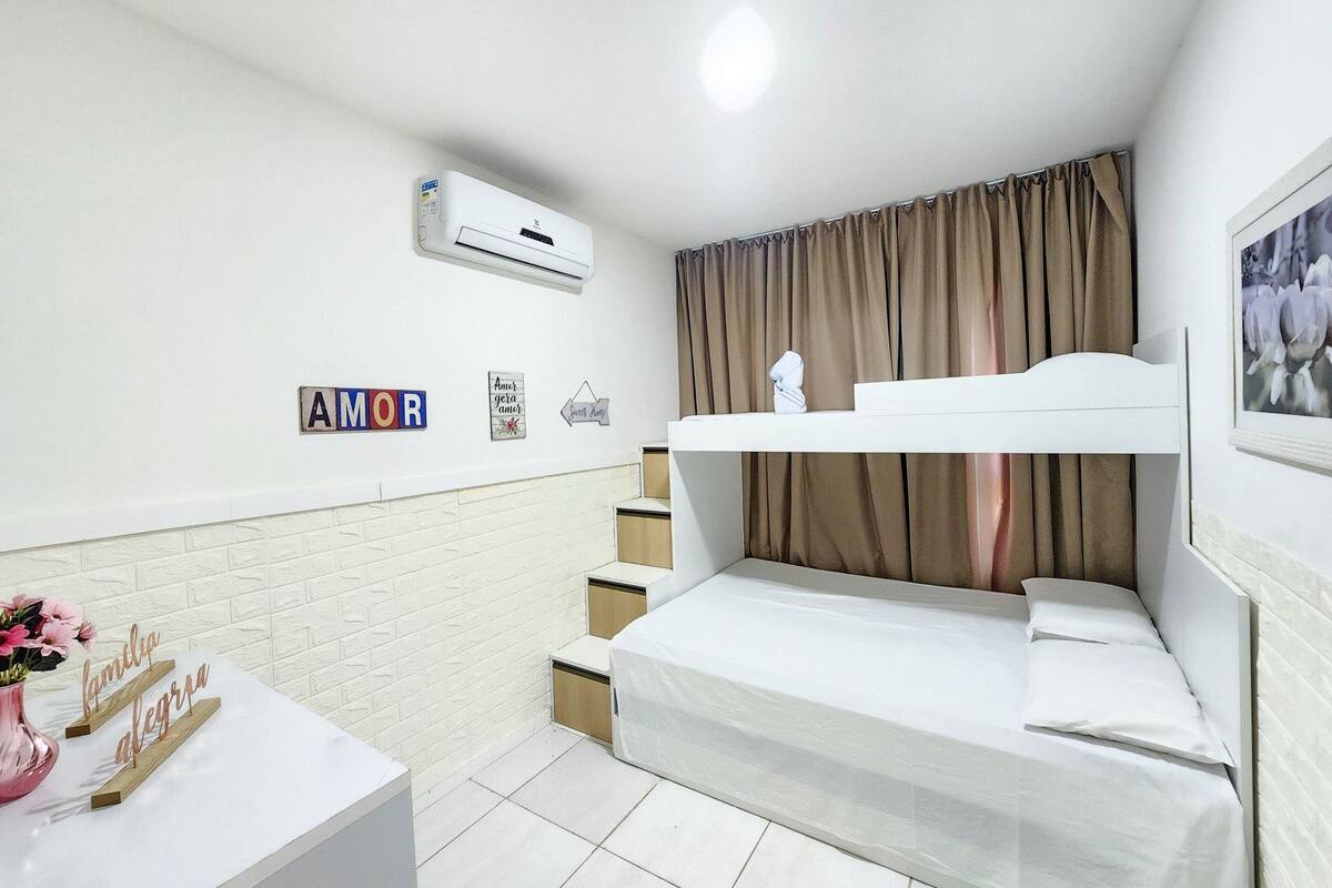 A bedroom with a bunk bed, a white desk, a vase with flowers, and a wall-mounted air conditioner.