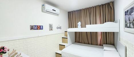 Een slaapkamer met een stapelbed, een wit bureau, een vaas met bloemen en een luchtverkoeler aan de muur.