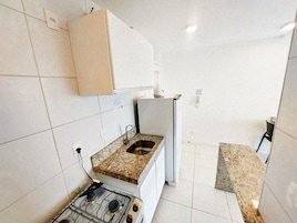 Una cocina compacta con paredes de azulejos blancos, encimera de granito, estufa a gas integrada y refrigerador blanco.