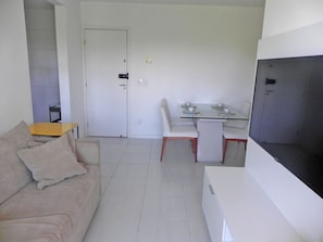 A living room with a sofa, a small table, a dining table with chairs, and a television.