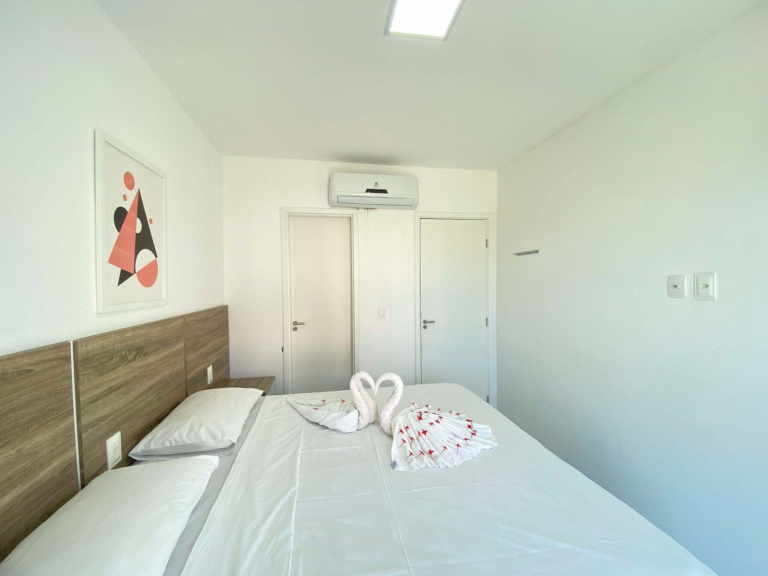 A hotel room with a bed, two doors, an air conditioning unit, and a framed picture on the wall.