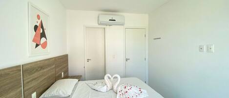 A hotel room with a bed, two doors, an air conditioning unit, and a framed picture on the wall.