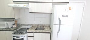 A kitchen with a gas stove, microwave, sink, and a white refrigerator.