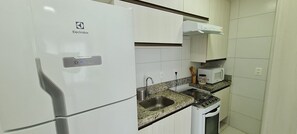 A kitchen with a white Electrolux refrigerator, a granite countertop, a stainless steel sink, a stove, and a microwave.