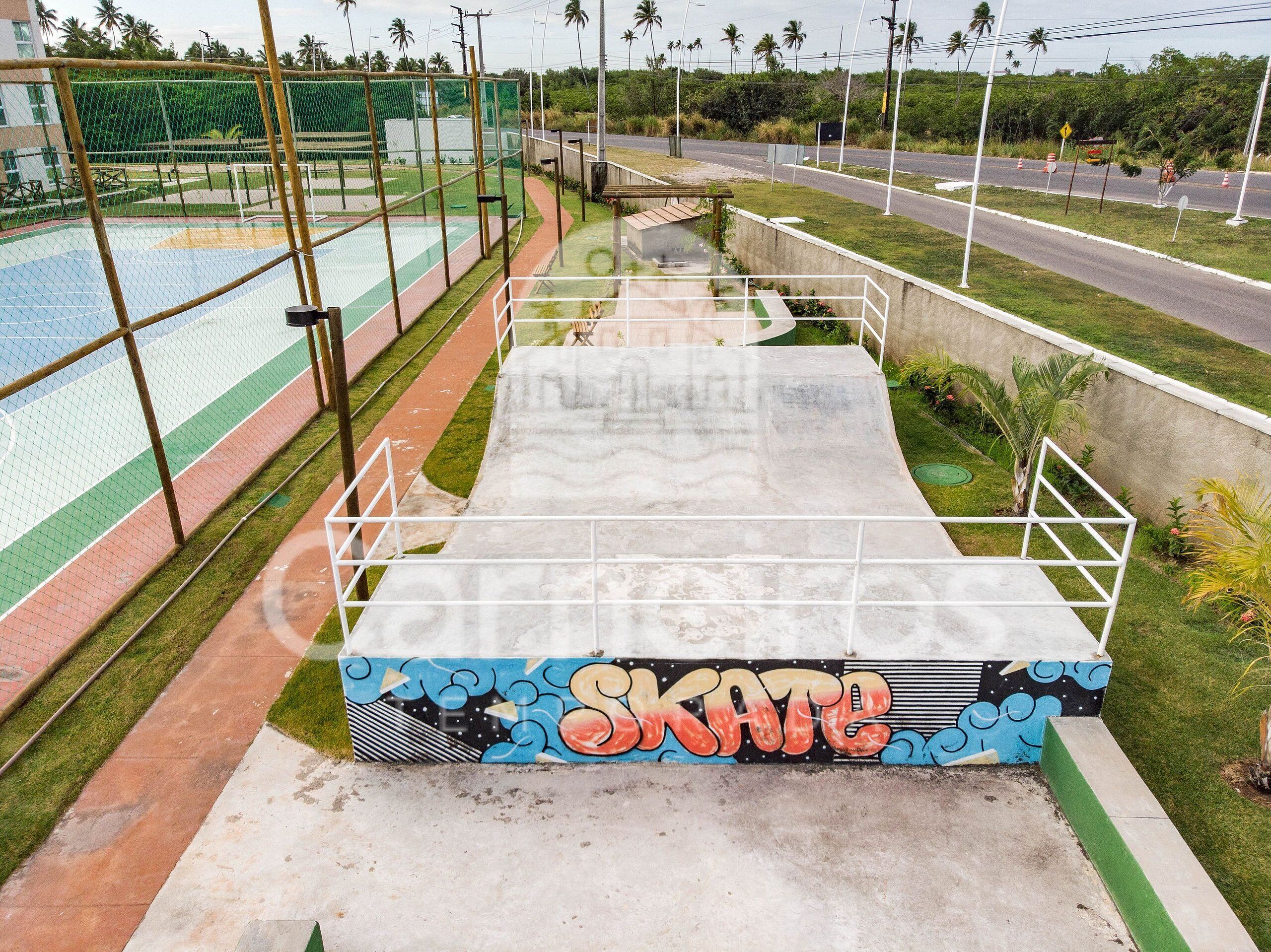 Un parc à skate avec une rampe, une zone délimitée par une clôture et une route avec des panneaux de signalisation.