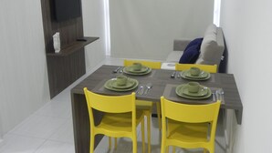 A dining area with a table set for four, yellow chairs, and a grey sofa in the background. - Flats no Muro Alto Condomínio Club (Ipojuca)
