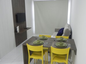 Uma área de refeições com uma mesa posta para quatro pessoas, cadeiras amarelas e um sofá cinza ao fundo.