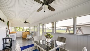 Une pièce spacieuse avec une table en verre, des chaises en osier et un ventilateur de plafond.