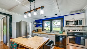 Une cuisine moderne dotée d’un îlot central en bois, d’appareils électroménagers en acier inoxydable et offrant une vue sur l’extérieur.