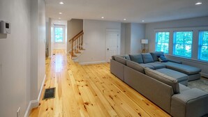 A spacious living area with a wooden floor, a grey sectional sofa, and a staircase leading to another room. - Yarmouth Port Escape Minutes to the Beach (Yarmouth)