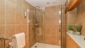 A modern bathroom with a glass-enclosed shower, a white toilet, and a wooden vanity with potted plants.